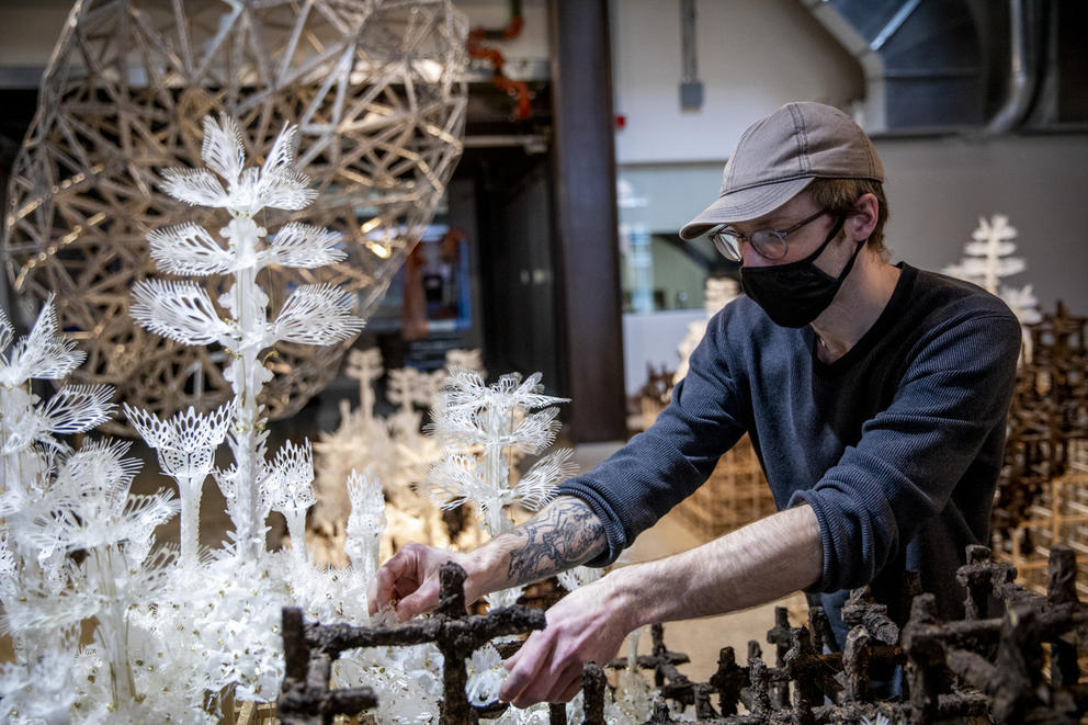 person with dark mask working on white flowers on artwork