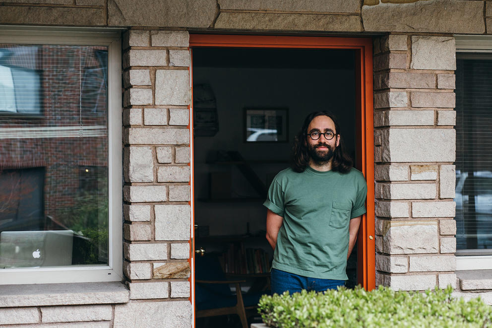 A man with long hair and green t-shirt on his doorstep