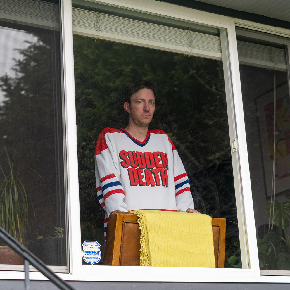 Person behind window, wearing a white t-shirt with the text "sudden death"