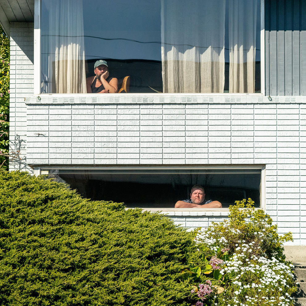 Front of a house with two windows, one person in each of them
