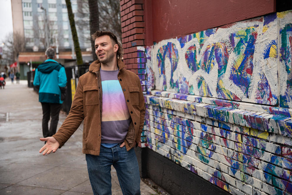 Man gestures next to colorful mural