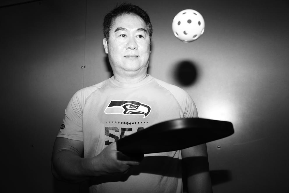 A close up of a man bouncing a pickleball on a paddle