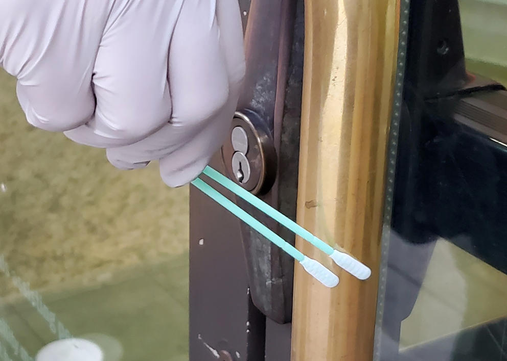 gloved hand holding swabs and swabbing a door handle 