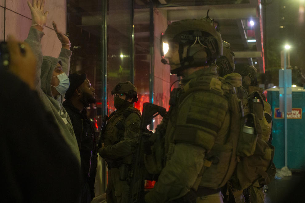 Police in tactical gear talk to demonstrators with their hands up
