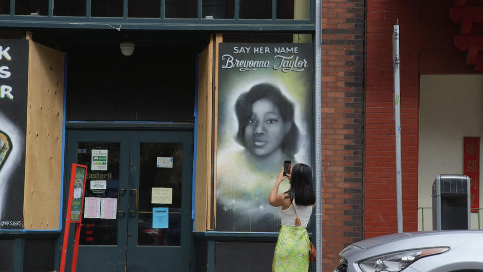 A woman holds her photo up to a painted plywood mural