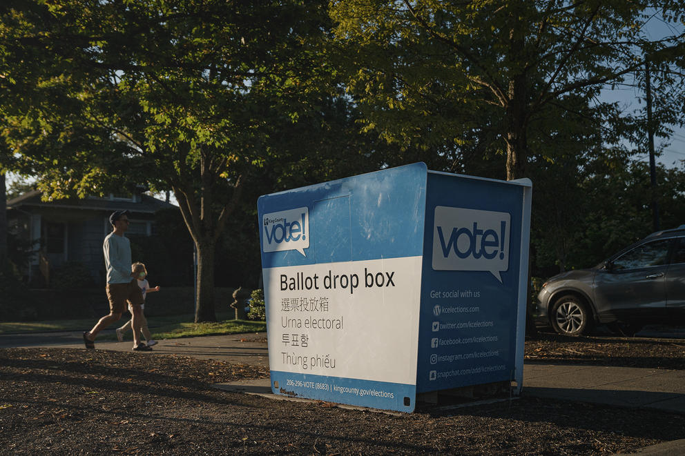 A father and his daughter walk by a ballot drop box