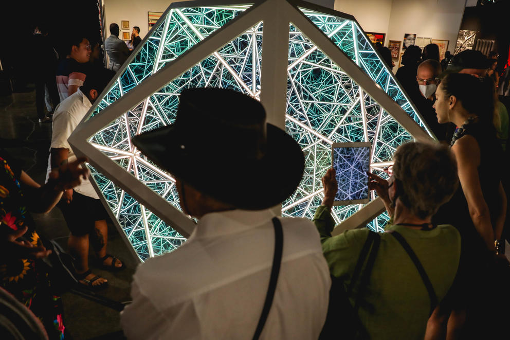 a man in a cowboy hat stands in front of a large, lit up art installation