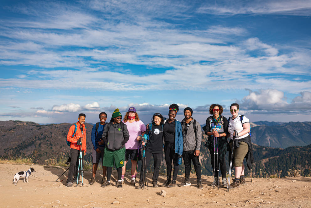 A group of nine hikers and a dog pose for a photo at a viewpoint