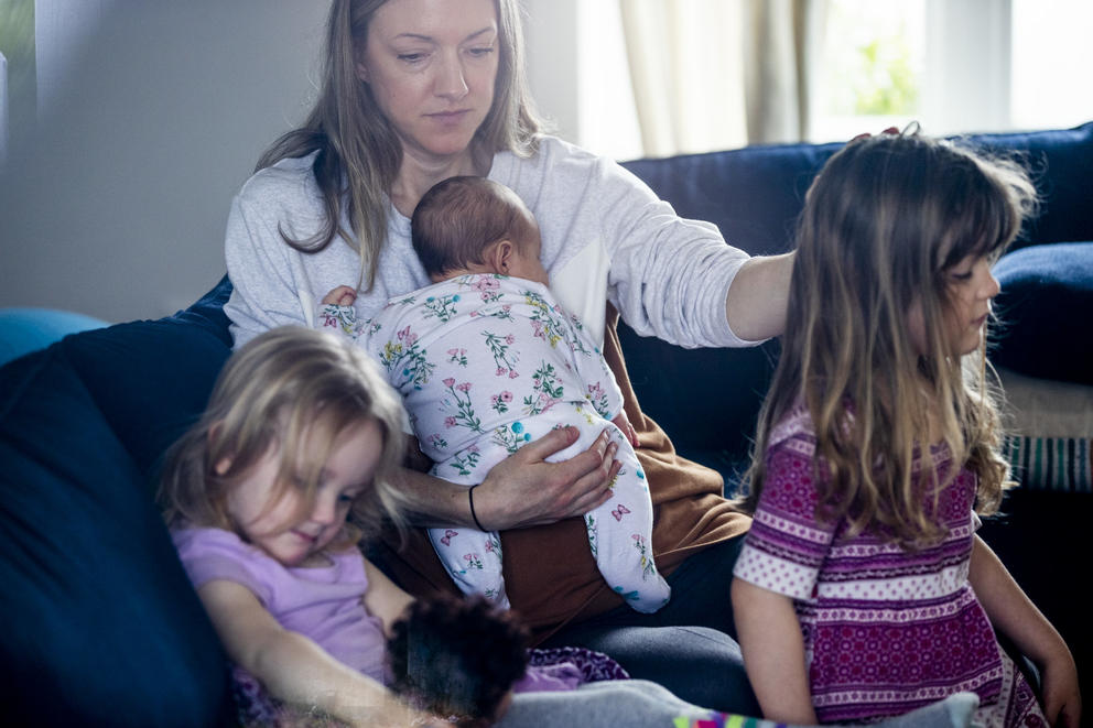 A mother playing with her two daughters while holding a baby