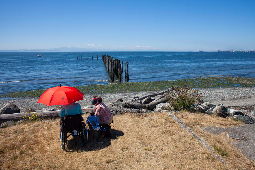 Two people sit in chairs along the short beneath an umbrella