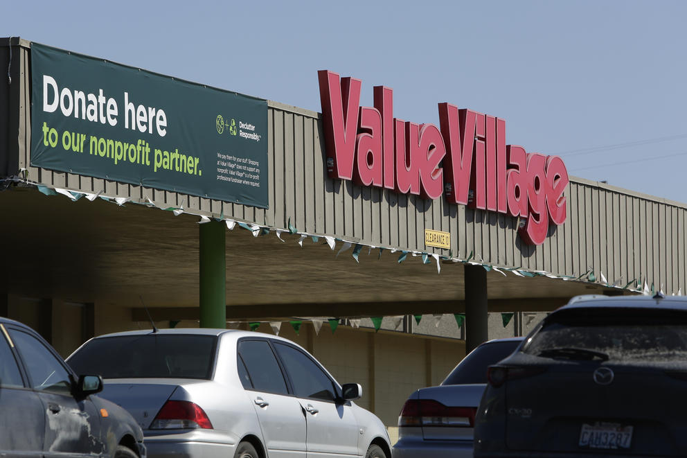 a line of cars in a value village parking lot near a banner that reads "donate here to our nonprofit partner"