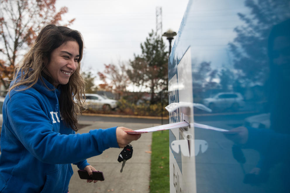 a woman puts her ballot in a ballot drop box