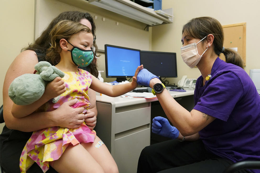 A mother holds her toddler during an appointment with a nurse