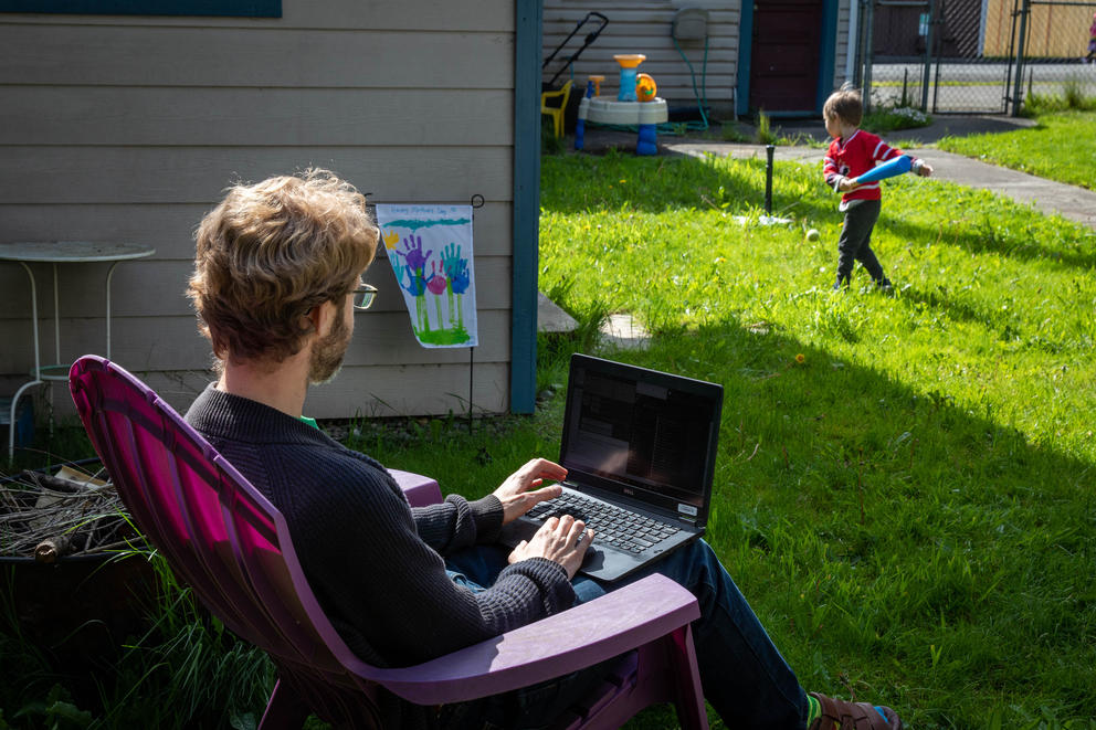 Ryan Webber sits in a deck chair in the grass, watching his son play in the background.