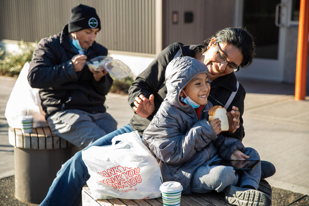 a man, woman, and little boy eat a meal outside in the sun