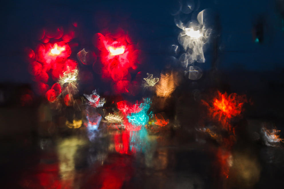 Street lights are blurred as seen through the rain on a windshield
