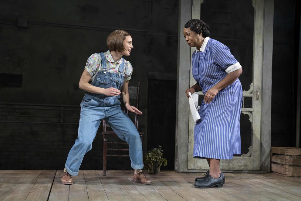 A young white girl in overalls stands to the left, to the right an older Black woman in a blue dress
