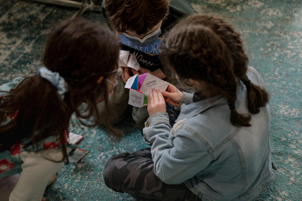 Students sit on the floor with brightly colored paper with questions in Spanish.
