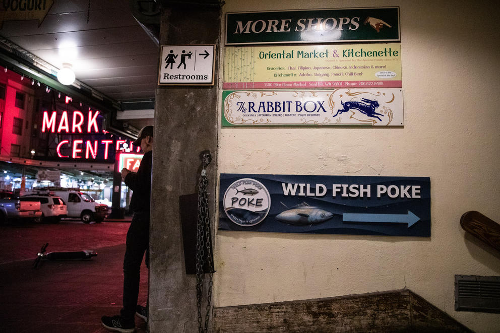 man stands near a wall that has a variety of signs on it, including one saying "Rabbit Box"