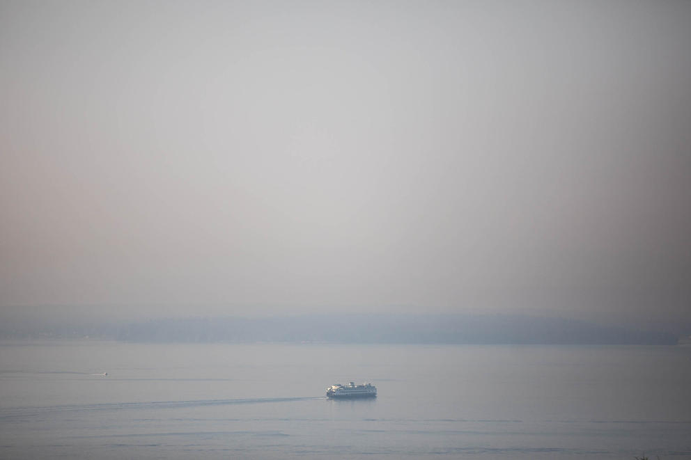 A ferry wades through wildfire smoke in the foreground of mountains 
