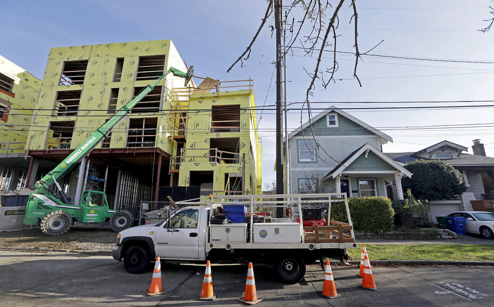 a four story apartment building is under construction next to a single family house. a construction vehicle is in the foreground