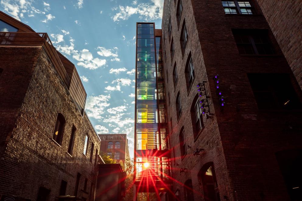 two brick buildings with a stairwell lit in rainbow colors in between