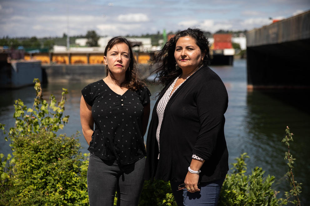 two people are standing in front of a river, looking at the camera. 