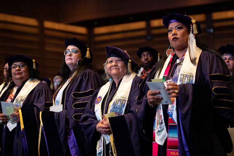 A group of university graduates stand in doctoral regalia during a commencement ceremony.