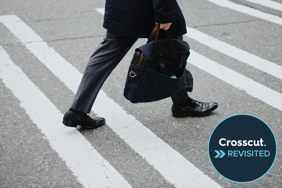 a close up of a man's legs and briefcase walking across a sidewalk