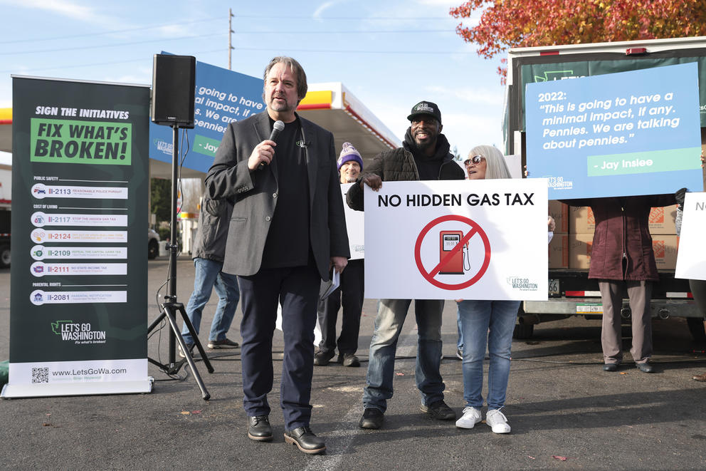A man with a microphone stands with a group of demonstrators holding signs