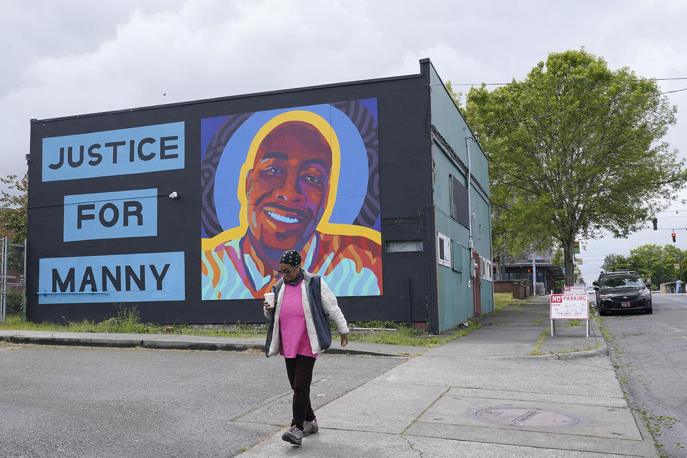 A person walks past a mural that says "Justice for Manny" next to a smiling portrait of Manuel Ellis.