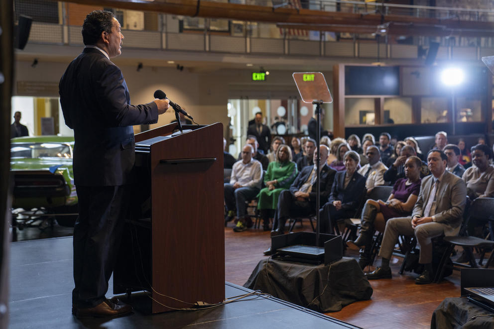 a man stands at a podium on a stage speaking to an audience 