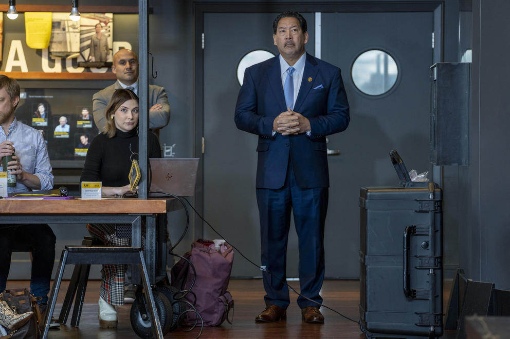 a man stands to the right of a woman and man sitting at a table