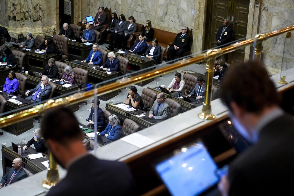 People sitting in a balcony observe a gallery below where others sit at desks. 