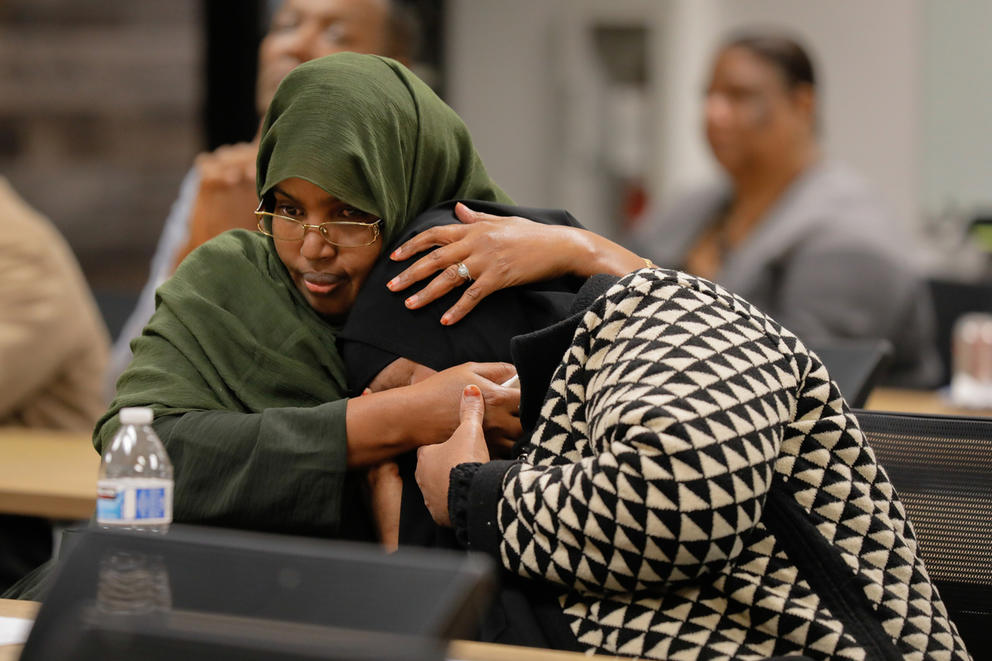 two women are sitting next to each other. one woman crys into the arms of the other