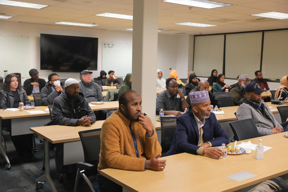 three rows of people sitting at long tables in a meeting room