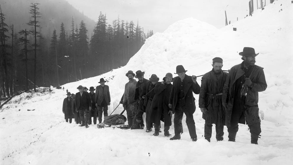Men pull a wrapped body through the snow.