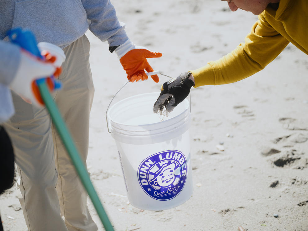 A hand holds out a bucket while another hand enters the frame to throw trash into it