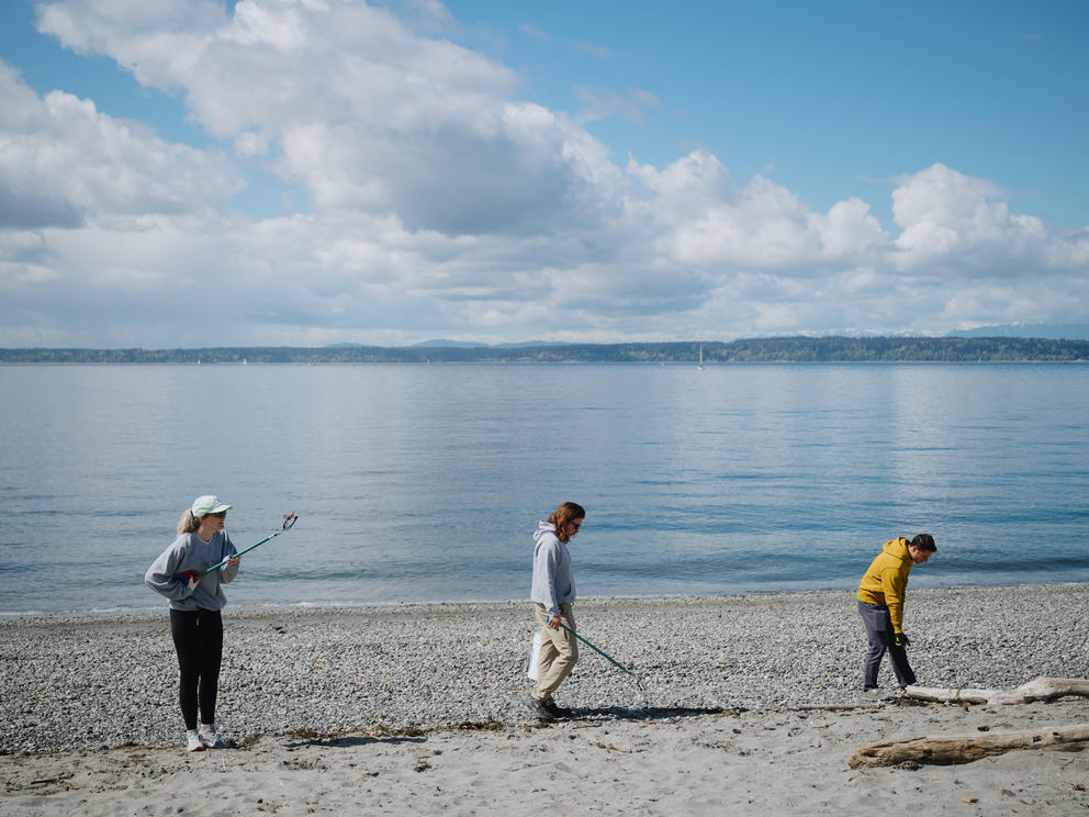 three people pick up trash on the beach