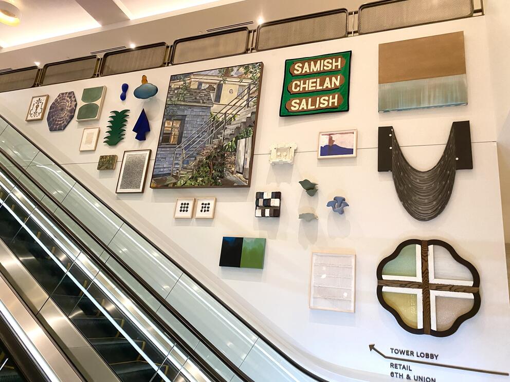 photo of an escalator next to a wall of many different small artworks