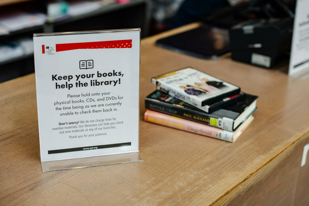 A sign on a shelf asks patrons to keep their books, CDs and DVDs because the library cannot currently check them back in.