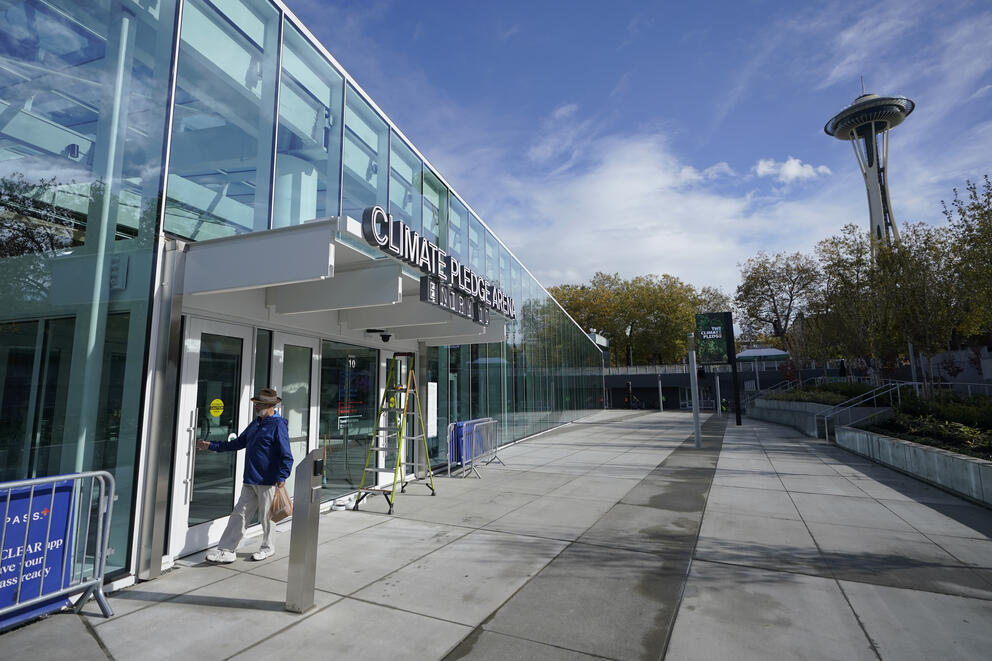 A person reaches for the handle of a glass door of an entrance labeled "Climate Pledge Arena Entry 10." The Space Needle is in the background.