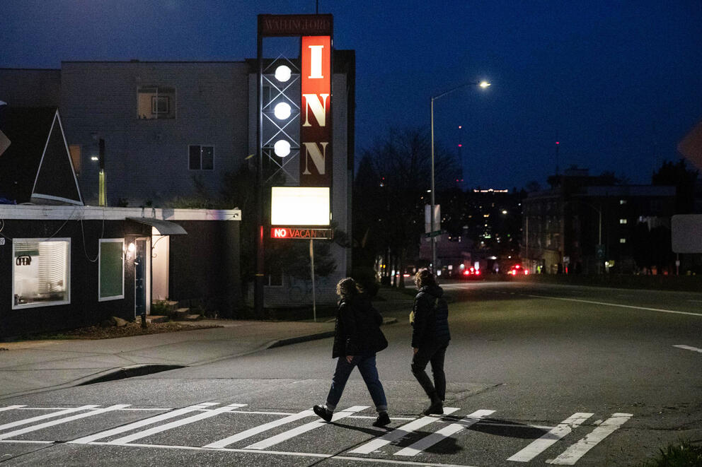 silhouettes of two people walking across a wide street at night 