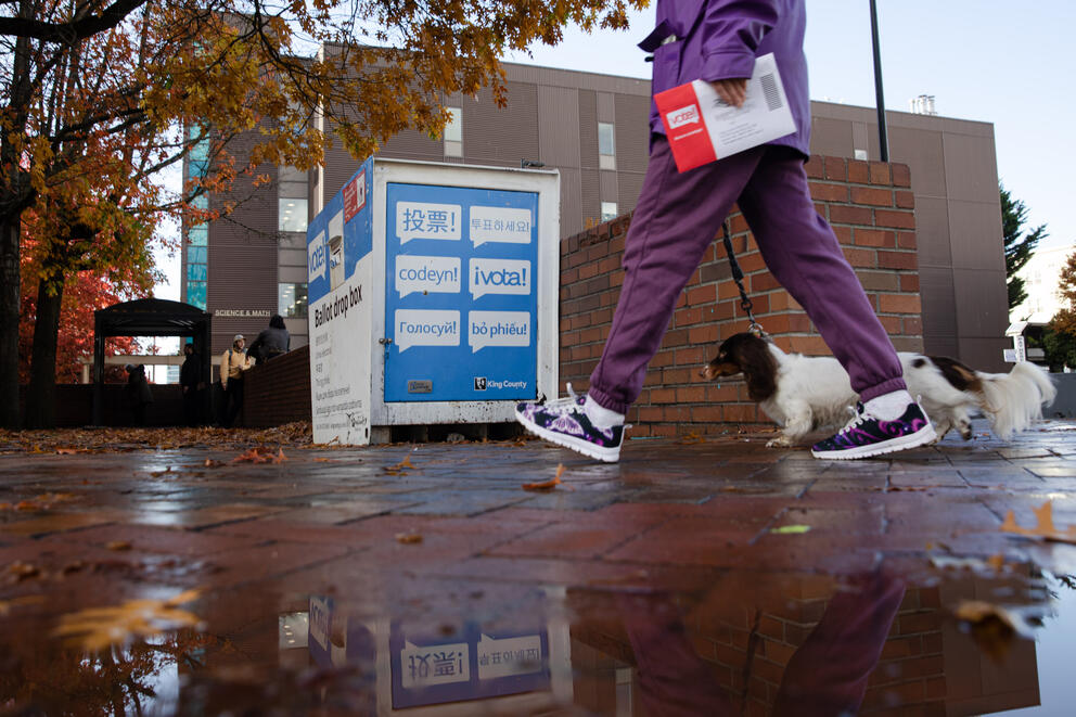 feet walking through a puddle near a ballot drop box