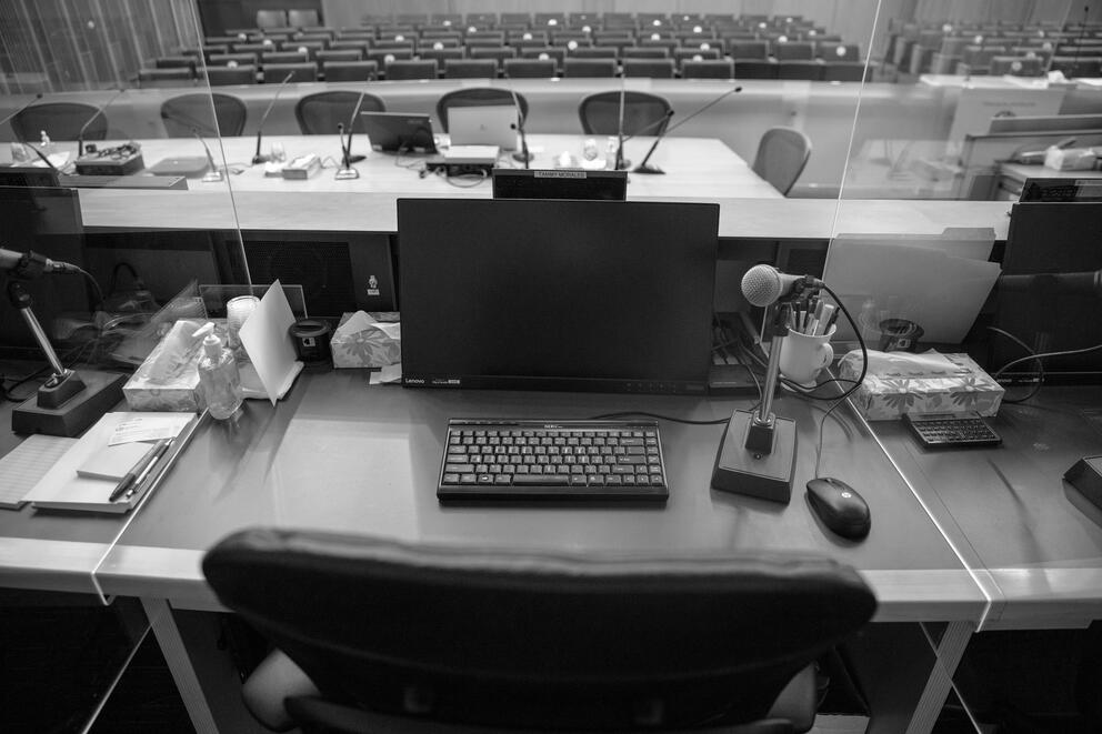 a computer sits on an empty councilmember desk looking out over empty seats in the council chambers