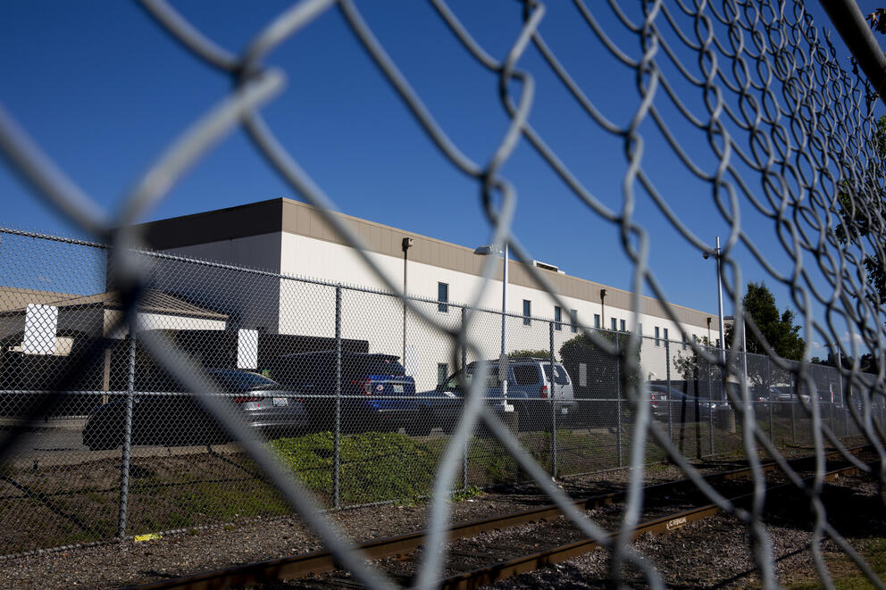 a close up image of a fence with a detention facility in the background