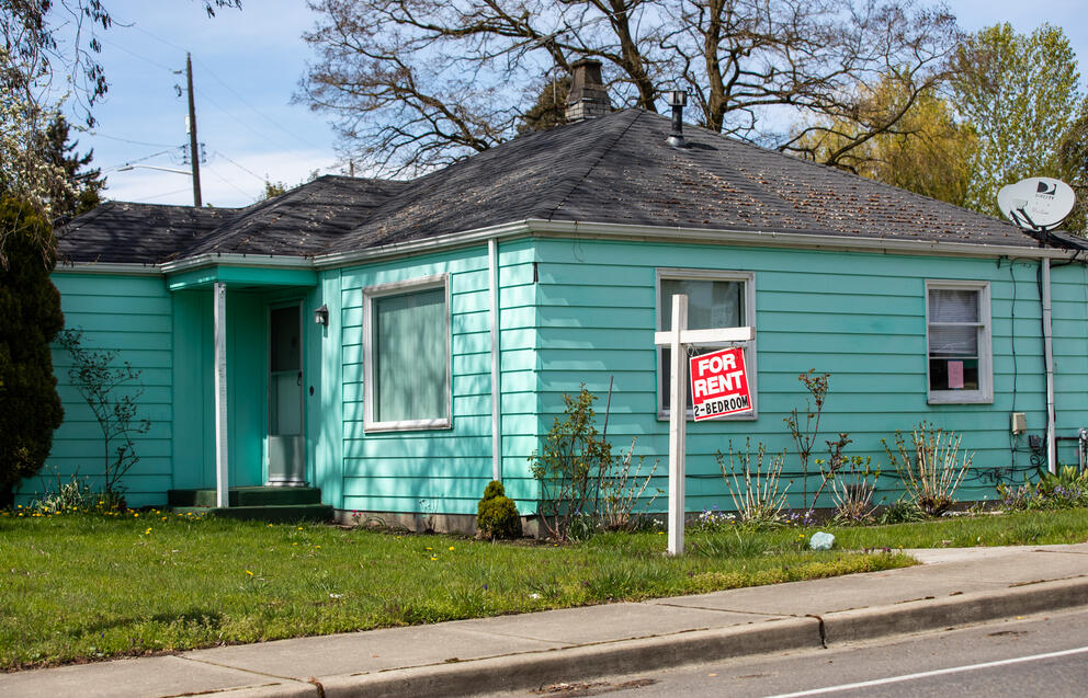 A green house has a sign out front that says "For Rent, Two Bedrooms"