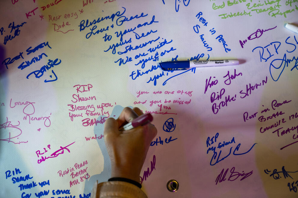 a hand holding a sharpie signs a poster with remembrances 