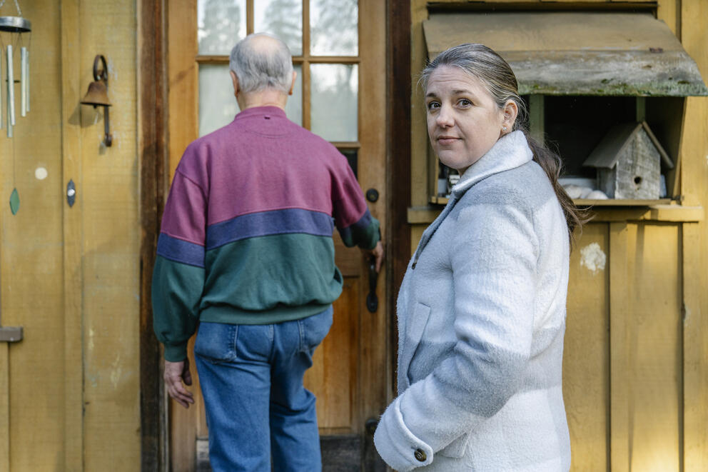 A person faces the camera, while an older person's back is to the camera.