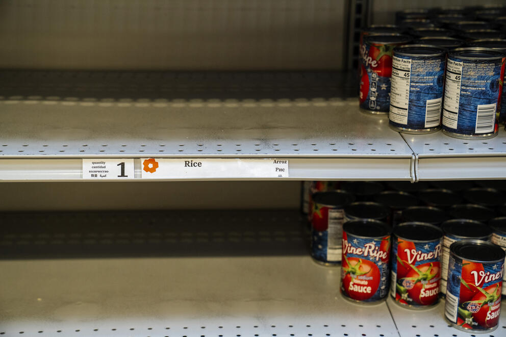 a mostly empty shelf at a food bank with a few cans of vegetables 